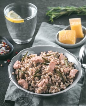 Raw buckwheat risotto with chicken meat and rosemary served parmesan cheese in gray plate on black cement background. Gluten-free and buckwheat recipe ideas. Copy space. Toned image.