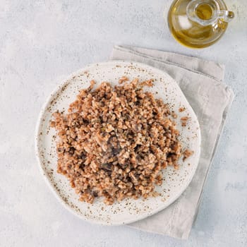Buckwheat risotto with dried mushrooms in craft plate on light gray or white cement background. Gluten-free and vegetarian buckwheat recipe ideas. Copy space. Top view or flat-lay.