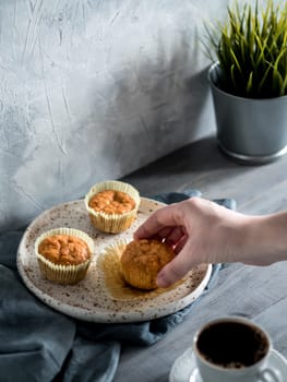 Homemade muffins on craft plate over gray wooden table. Hand hold carrot cupcake. Copy space. Toned image in scandinavian style.