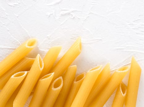 Raw pasta as food background. Italian Penne Rigate Macaroni Pasta on textured white background. Dried pasta selection close up. Top view or flat lay with copy space