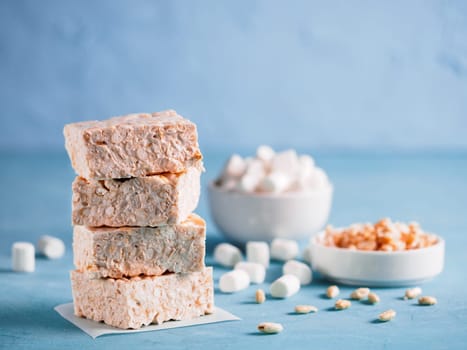 Homemade square bars of marshmallow and crispy rice with ingredients on blue background. Stack of American dessert with marshmallow and crispy rice. Copy space