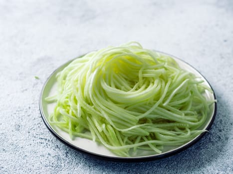 Zucchini noodles on plate. Vegetable noodles - green zoodles or courgette spaghetti on plate over gray stone background. Clean eating, raw vegetarian food concept. Copy space for text.