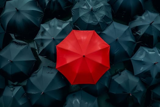 A vibrant red umbrella stands out among a group of black umbrellas in a crowded setting.