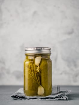 Glass jar with pickled cucumbers on gray background with copy space for text. Perfect homemade marinated cucumbers in mason jar on rustic table. Vertical.