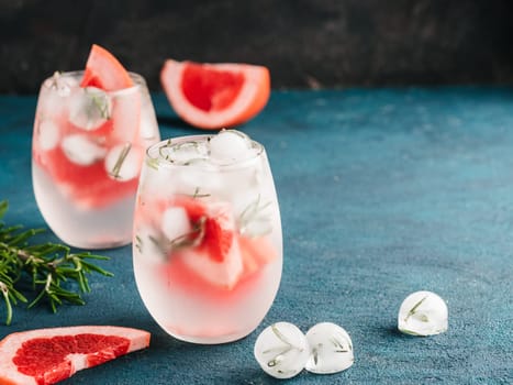 infused detox water or alcoholic or non-alcoholic cocktail with grapefruit and rosemary ice in glass on green and black cement background. healthy eating or holyday drink concept, copy space for text