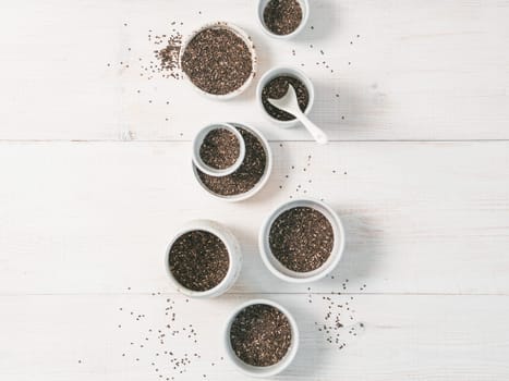 Organic chia seeds on white wooden table. Set of small bowls with organic chia seed. Superfood concept. Copy space. Top view or flat-lay.