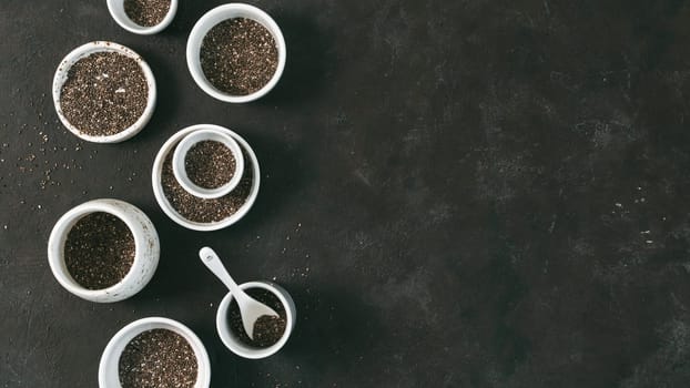 Organic chia seeds on black tabletop. Set of small bowls with organic chia seed. Superfood concept. Copy space. Top view or flat-lay. Banner