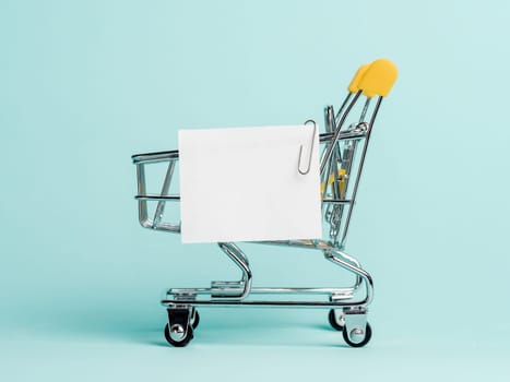 Shopping cart and white paper note list over blue background. Shopping concept on blue background. Empty white paper note over shopping cart. Copy space for text or design.