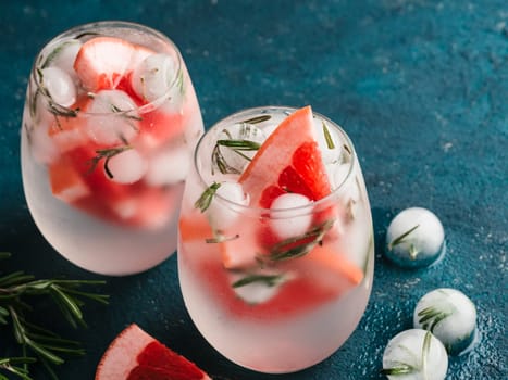 infused detox water or alcoholic or non-alcoholic cocktail with grapefruit and rosemary ice in glass on green cement background. healthy eating or holyday drink concept, copy space for text.