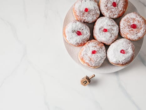 Jewish holiday Hanukkah concept and background. Hanukkah food doughnuts and traditional spinnig dreidl or dredel on white marble table background. Copy space for text. Shallow DOF.Top view or flat lay