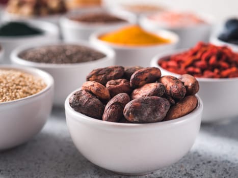 Raw cocoa bean in small white bowl and other superfoods on background. Selective focus. Different superfoods ingredients. Concept and illustration for superfood and detox food