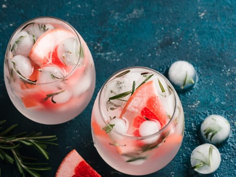 infused detox water or alcoholic or non-alcoholic cocktail with grapefruit and rosemary ice in glass on green cement background. healthy eating or holyday drink concept, copy space for text.