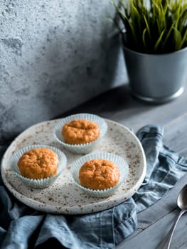 Homemade muffins on craft plate over gray wooden table. Carrot cupcakes with copy space. Toned image in scandinavian style. Copy space. Toned image in scandinavian style.