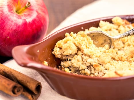 Homemade apple cramble cake with fresh apples and cinnamon sticks on rustic dark wooden background