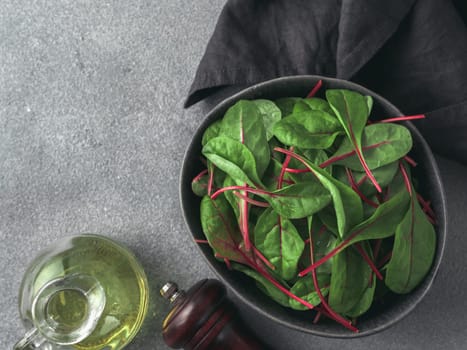 Fresh salad of green chard leaves or mangold on gray stone background. Flat lay or top view fresh baby beet leaves in craft ceramic bowl.