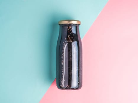 Detox activated charcoal black chia water or mocktail on colorful blue and pink background. Bottle with black chia infused water.Detox drink idea and recipe.Vegan food and drink.Top view