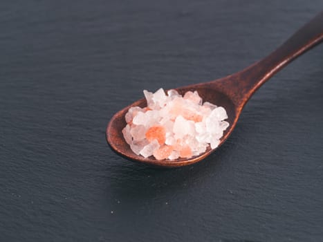 Himalayan pink salt in spoon on black stone background. Copy space