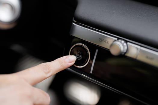 Pressing Stand By Power Button To Turn On and Off the Electric Car Close-Up. Push start stop button of ev car. Finger press the button to start the car engine. Concept of transportation and technology.