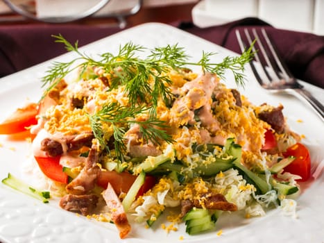 Close up view of salad with bacon, cucumber, pepper and dressed with egg. Salad in white plate on dark brown wooden table in restaurant