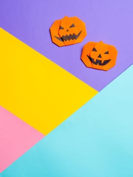 Halloween concept. Paper origami pumpkin on colorful background. Simple idea for halloween - easy made paper pumpkins on multicolor blue, yellow, pink, lilac background. Copy space for text. Vertical