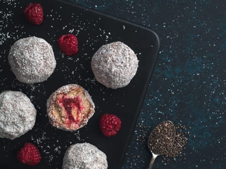 Raw vegan lamington bliss balls with raspberries chia jam on dark background. No baked healthy vegan sweet dessert idea and recipe. Copy space for text. Top view or flat-lay.