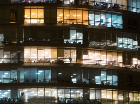 Window of the multi-storey building of glass office lighting and working people within. Windows office building for background. People working late