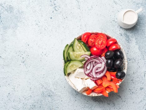 Greek Salad Bowl on gray cement background, copy space. Above view of Bowl Greek Salad and dressing sauce. Trendy food. Idea, recept and concept of modern healthy food.