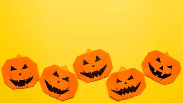 Halloween concept. Paper origami pumpkin on yellow background. Simple idea for halloween - easy made paper pumpkins on trendy color Ceylon Yellow background. Copy space for text. Banner