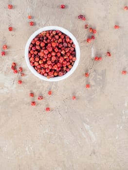 Pile with dried pink pepper berries on brown concrete background. Close up view of pink peppercorn. Top view or flat-lay. Copy space.