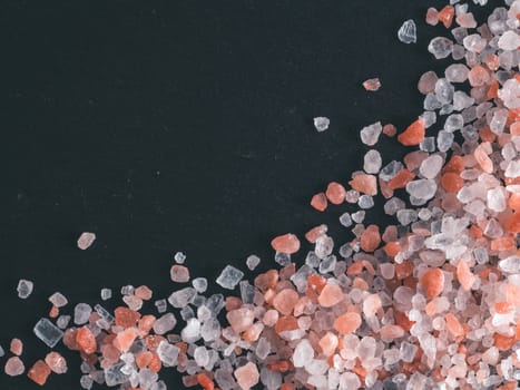 Himalayan pink salt in crystals on black stone background. Copy space