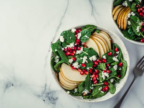 Fresh salad with baby spinach, pear, pomegranate and cottage cheese. Two bowls with delicious summer fruit salad on marble table. Copy space for text. Ideas and recipes for healthy breakfast or lunch