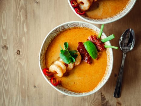 Tom yam kong ready-to-eat. Tom yum soup with shrimps on wooden table. Popular spicy Thai dish Tom Yam top view. Thailand food and Thai cuisine. Copy space for text. Natural day light