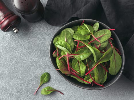 Fresh salad of green chard leaves or mangold on gray stone background. Flat lay or top view fresh baby beet leaves in craft ceramic bowl.