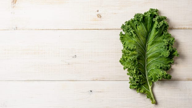 Fresh green kale leaf on white wooden tabletop, copy space left. Flat lay or top view. Healthy detox vegetables. Clean eating and dieting concept. Health kale benefits. Banner