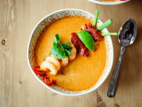 Tom yam kong ready-to-eat. Tom yum soup with shrimps on wooden table. Popular spicy Thai dish Tom Yam top view. Thailand food and Thai cuisine. Natural day light
