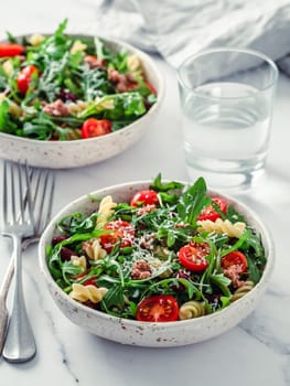 Warm salad with tuna, arugula, tomatoes, red bean, pasta. Idea and recipe for healthy lunch or dinner. Two bowls with warm salads on marble tabletop. Ideas and recipes for healthy dinner or lunch