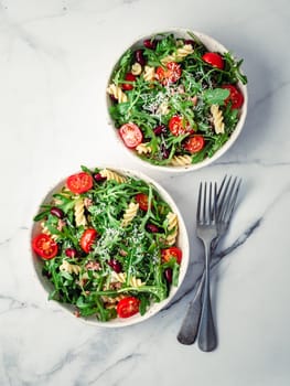 Warm salad with tuna, arugula, tomatoes ,red bean, pasta.Idea and recipe for healthy lunch or dinner.Two bowls with warm salads on marble table. Ideas and recipes for healthy dinner or lunch. Vertical
