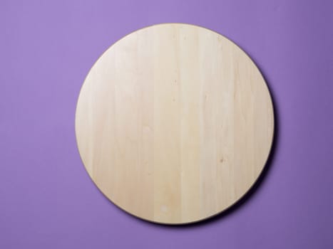 Empty wooden round tray or trencher, cutting board on lilac background. Hard light. Top view or flat lay.