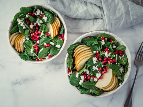 Fresh salad with baby spinach, pear, pomegranate and cottage cheese. Two bowls with delicious summer fruit salad on marble table. Copy space for text. Ideas and recipes for healthy breakfast or lunch