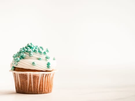 Cupcake decorated blue sprinkles and copy space right. White marble background.