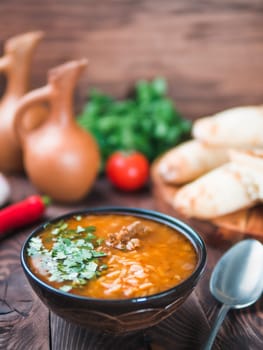 Traditional Georgian kitchen-soup Kharcho with meat,rice and fresh cilantro.Spicy soup Kharcho on wooden table with traditional bread Shotis Puri,vintage wine jar,vegetables.Copy space text. Vertical.