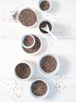 Organic chia seeds on white wooden table. Set of small bowls with organic chia seed. Superfood concept. Copy space. Top view or flat-lay. Vertical.