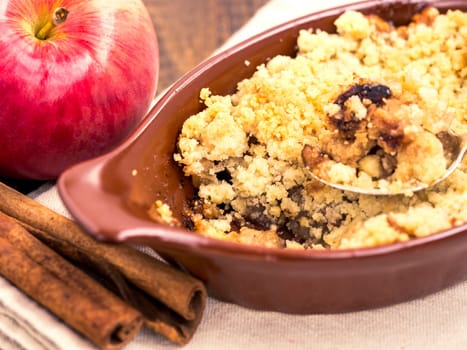 Homemade apple cramble cake with fresh apples and cinnamon sticks on rustic dark wooden background