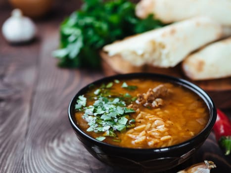 Traditional Georgian kitchen-soup Kharcho with meat, rice and fresh cilantro. Spicy soup Kharcho on wooden table with traditional bread Shotis Puri and vegetables. Selective focus. Copy space for text