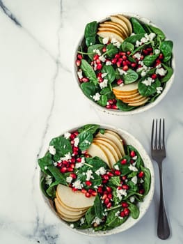 Vegan salad bowl with spinach, pear, pomegranate, cheese on marble tabletop. Vegan breakfast, vegetarian food, diet concept. Vertical. Top view or flat lay.