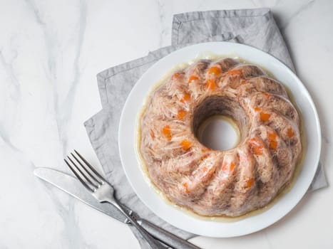 Homemade delicious jelly meat on white marble table. Perfect jellied meat, aspic, galantine with carrot. Copy space for text. Top view or flat lay.