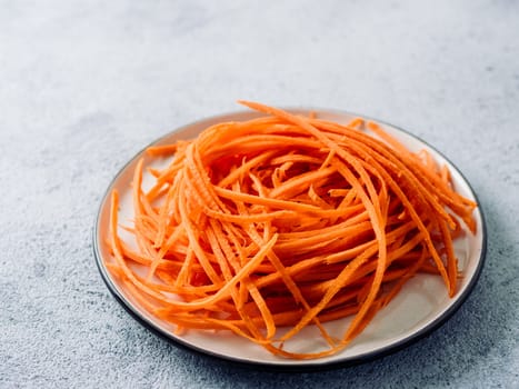 Carrot noodles on plate. Vegetable noodles - orange sweet carrot spaghetti on plate over gray cement background. Clean eating, raw vegetarian food concept. Copy space for text.