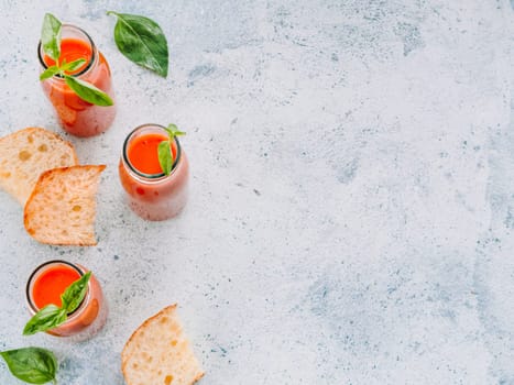 Delicious gaspacho soup in glass bottles. Traditional spanish cold soup puree gaspacho or gazpacho on gray cement background with copy space for text. View from above or top view or flat lay