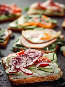 Close up view of different sandwiches with salami, vegetables and black sesame. Copy space for text. Assortment meat toasts on black background. Idea, creative concept for sausage maker. Vertical