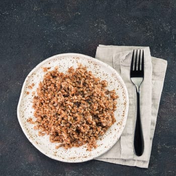 Buckwheat risotto with dried mushrooms in craft plate on black cement background. Gluten-free and vegetarian buckwheat recipe ideas. Copy space. Top view or flat-lay.
